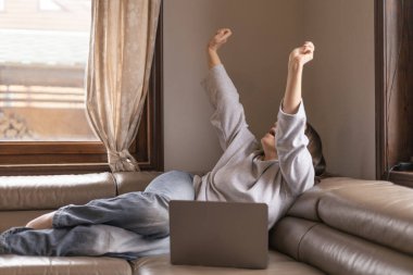 Bir kadın dizüstü bilgisayarının önünde kanepede uzanırken esniyor.