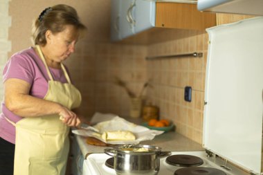 Kıdemli kadın tavaya tereyağı koyuyor.