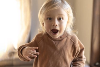 Üç yaşında sarı saçlı bir çocuk evdeki kanepede zıplayıp duruyor.