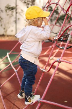 Üç yaşında bir çocuk, halka açık bir oyun alanının duvarında tırmanma pratiği yapıyor..
