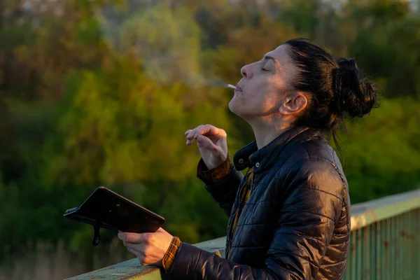 Uma Mulher Está Uma Ponte Fuma Cigarro Segurando Smartphone Suas — Fotografia de Stock