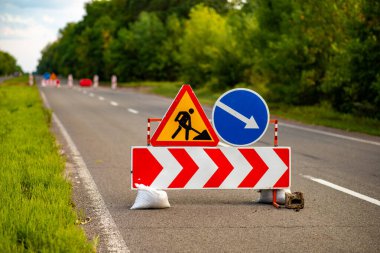 Yol tabelaları ileride inşaat çalışması olduğunu gösteriyor, sürücüleri sapma ve güvenlik önlemlerine karşı uyarıyor. Trafik yönetimi, kentsel gelişim veya altyapı projelerini resmetmek için ideal. Herhangi bir taşımacılık veya inşaatla ilgili içerik için hayati bir görüntü.