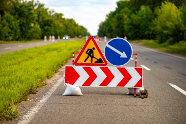 Yol tabelaları ileride inşaat çalışması olduğunu gösteriyor, sürücüleri sapma ve güvenlik önlemlerine karşı uyarıyor. Trafik yönetimi, kentsel gelişim veya altyapı projelerini resmetmek için ideal. Herhangi bir taşımacılık veya inşaatla ilgili içerik için hayati bir görüntü.