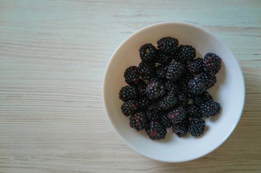 Beyaz bir kasede taze böğürtlen, lezzet ve besinlerle dolup taşıyor. Antioksidan, vitamin ve lif açısından zengin olan bu lezzetli böğürtlenler kalp sağlığını, bağışıklığı ve sindirim sistemini destekler. Bu görüntü başlığı, sağlık bilinci olan tüketiciler için mükemmel.