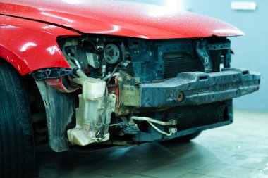 Kırmızı bir arabanın hasarlı ön tarafının yakın çekimi, kırık farları ve buruşuk kaputu işaretlemek, kaza sonrasını ve tamir ihtiyacını sembolize ediyor. Sigorta, otomobil tamiri veya güvenlikle ilgili konular için ideal.