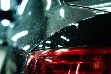 Parlak siyah bir araba gövdesinde parlayan yağmur damlaları dramatik ve zarif bir atmosfer yaratıyor. Hava, lüks ve otomotiv güzelliği temaları için ideal.