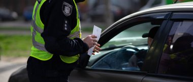 Bir Ukraynalı polis memuru, yol güvenliği ve toplum bilincini artırmak için el ilanı dağıtıyor. Bu görüntü bir etkileşim anını yakalayarak, kolluk kuvvetlerinin kamu güvenliği ve sivil çatışmadaki rolünü vurguluyor. Temaları resmetmek için ideal 