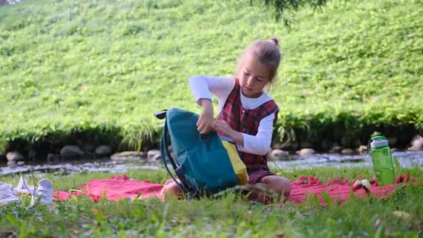 公園の女子高生が草の上に座り 本をリュックから出している 子供たちは学校に行く 子育てという概念は — ストック動画