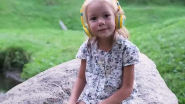 Una Niña Con Auriculares Escuchando Música Sentada Una Gran Piedra — Vídeos de Stock