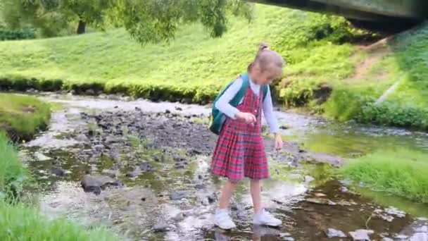 Seorang Gadis Sekolah Menyeberangi Sungai Menginjak Injak Batu — Stok Video