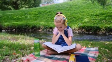 Küçük bir kız nehir kenarında oturmuş kitap okuyor.