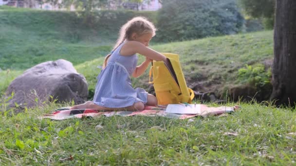 Młoda Dziewczyna Składa Materiały Szkolne Żółty Plecak Siedzi Trawie Parku — Wideo stockowe