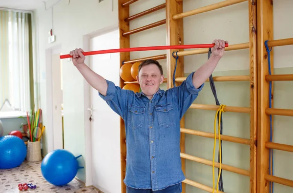 a young man with down syndrome is engaged in a gym with a gymnastic stick. rehabilitation process