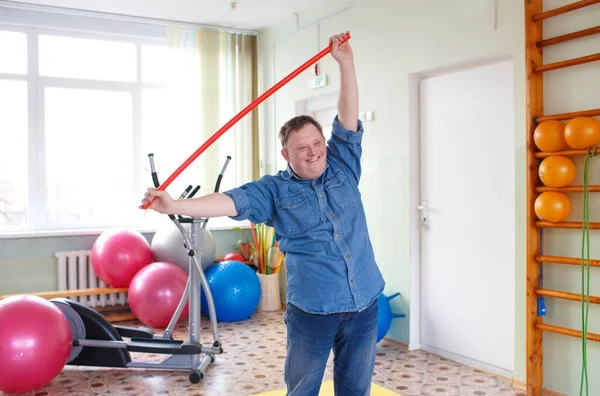 a young man with down syndrome is engaged in a gym with a gymnastic stick. rehabilitation process