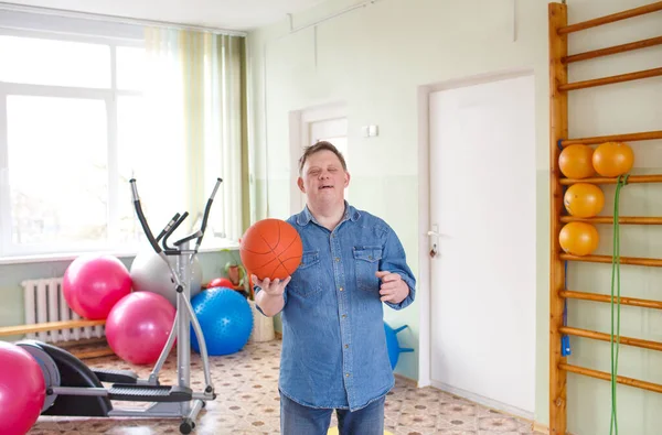 a man with down syndrome stands with a basketball in the gym