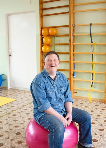 a man with down syndrome sits on a large inflatable ball in a rehabilitation center