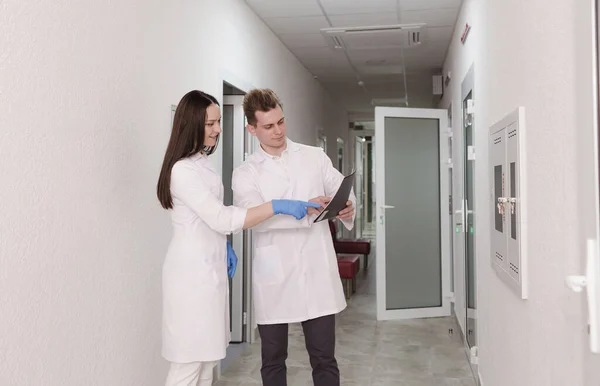 doctors discuss the medical report in the hospital. A young female doctor and a male doctor check the patient's clinical report online. Medical staff standing in the corridor of a private clinic.