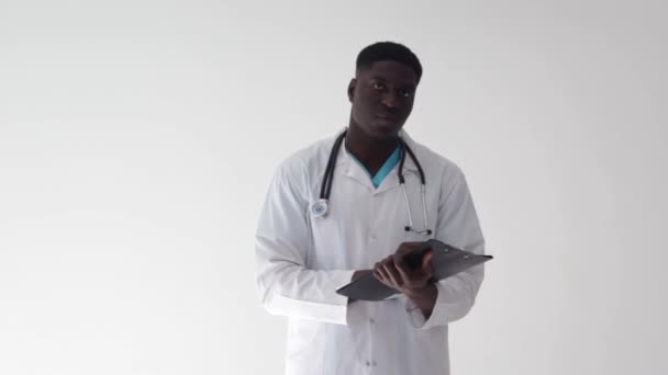 医療サービスの概念 患者の病歴を持つアフリカの笑顔の男の肖像とカメラで笑顔 光のスタジオの背景 — ストック動画