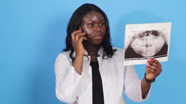 Afroamerykańska Lekarz Trzyma Rentgen Szczęki Rękach Rozmawia Przez Telefon Niebieskim — Wideo stockowe