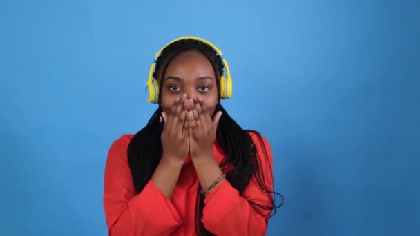 Africká Dívka Žlutých Sluchátkách Červené Šaty Fouká Polibek Modrém Pozadí — Stock video