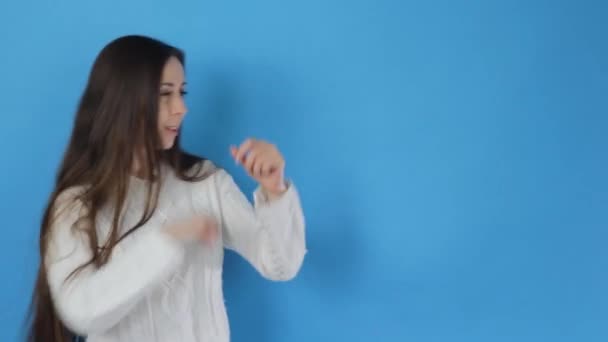 Een Brunette Meisje Danst Vrolijk Een Geïsoleerde Blauwe Achtergrond — Stockvideo