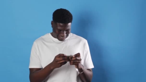 Ein Afroamerikanischer Mann Zockt Einem Smartphone Während Auf Blauem Hintergrund — Stockvideo