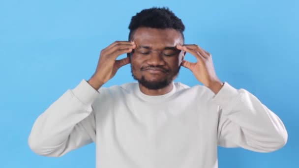 一位身穿白色T恤的健康的非洲裔美国年轻人按摩了他的太阳穴 患有头疼和偏头痛 一个封闭的工作室拍摄孤立在蓝色的背景 — 图库视频影像