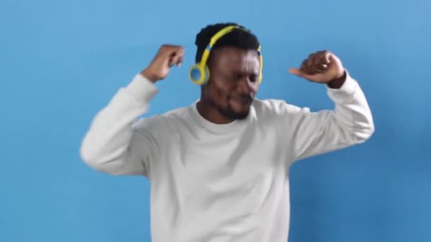Африканец Уганды Весело Танцует Желтых Наушниках Ритмичную Музыку Синем Фоне — стоковое видео