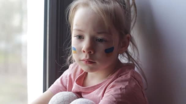 Smutna Dziewczynka Ukraińską Flagą Wymalowaną Twarzy Siedzi Patrzy Przez Okno — Wideo stockowe