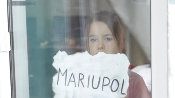 Mała Smutna Dziewczyna Spogląda Przez Okno Trzymając Kawałek Papieru Napisem — Wideo stockowe