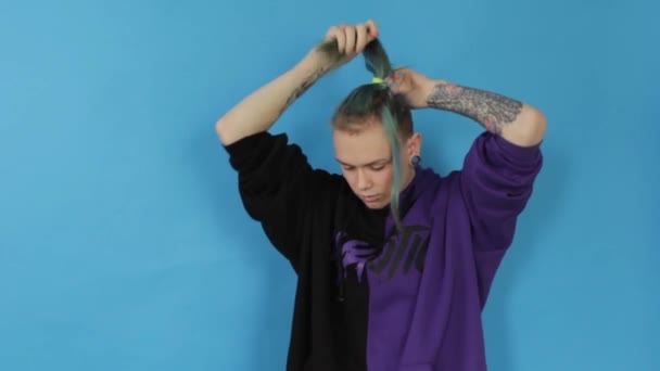 一个时髦的男女同性恋 双性恋和变性者男人把他的头发卷曲成头发 抽一支电子香烟 同时在蓝色背景下性感地释放烟雾 — 图库视频影像