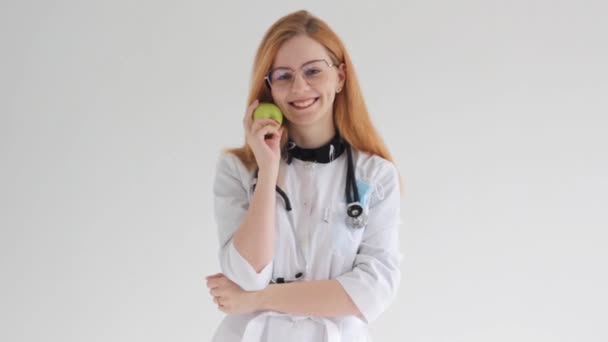 Uśmiechnięta Rudowłosa Lekarka Trzyma Jabłko Stetoskopem Izolacja Białym Tle — Wideo stockowe