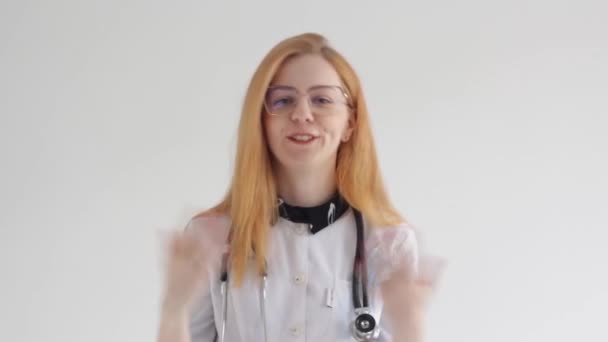 若い女の子の医者は白い背景でカメラを見ると言います — ストック動画