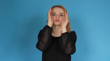 A close-up of an attractive young lady in , surprised and amazed, opened her mouth, raises her eyebrows, a shocked woman can't believe her eyes, looks into a camera isolated on a blue background