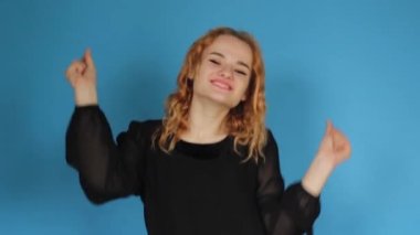 A teenage girl is dancing. Funny unusual red-haired girl having fun, hands up, grimacing, smiling, dancing in the studio on a blue background