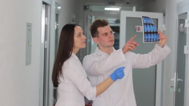 Δύο Νεαροί Γιατροί Εξετάζουν Αποτέλεσμα Μιας Αξονικής Τομογραφίας Στο Διάδρομο — Αρχείο Βίντεο