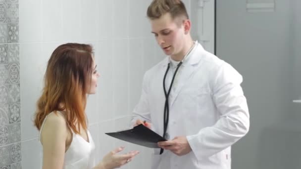 一名身穿白色医疗制服 面带微笑的年轻白人男医生在医院会面时与一位女性病人进行会诊 — 图库视频影像