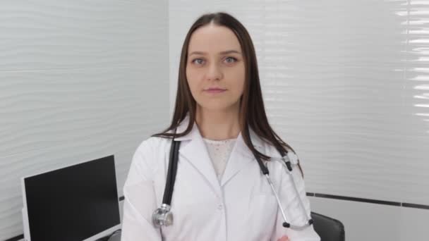 穿着白衣笑年轻的女医生 一位快乐的女医生 治疗师 全科医生站在医院时看着摄像机 — 图库视频影像