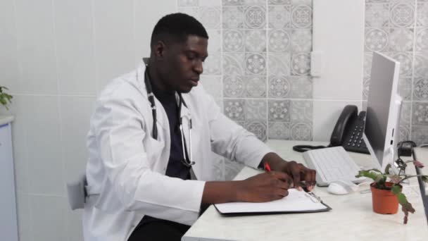 黑人医生在诊所的网上工作时做笔记 在检疫期间在网上咨询病人 — 图库视频影像