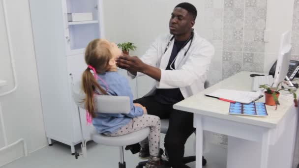 アフリカ系アメリカ人の医者は医務室で少女を注意深く検査する — ストック動画