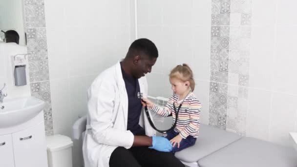 一个小女孩在办公室里和一位非裔美国医生一起玩 一个小孩在玩听诊器 — 图库视频影像