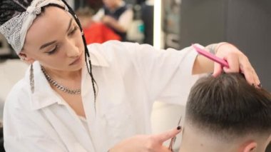 Stylish young girl hairdresser makes a haircut for a young man in a barbershop. She stands behind the client, finishing the job. Close-up.