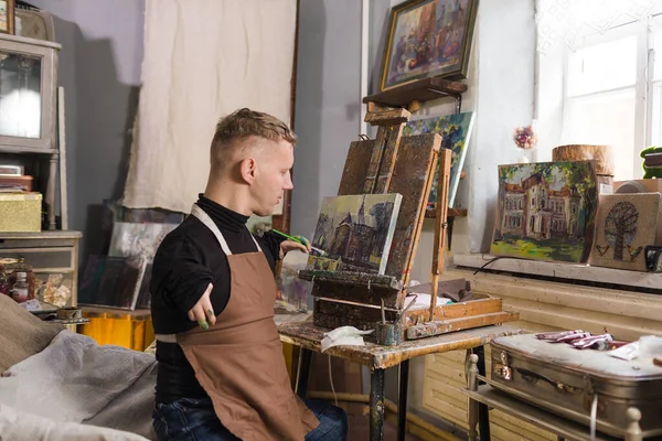 a young man with disabilities paints a picture with oil paints in an art workshop
