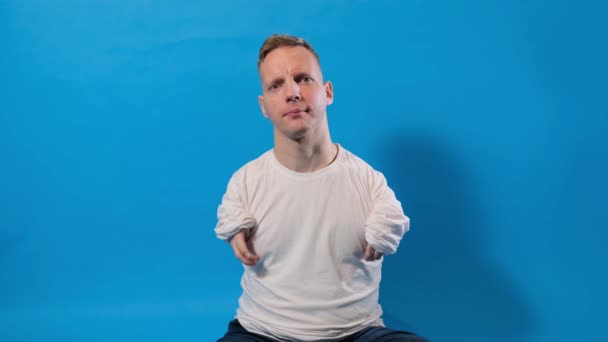 Ένας Άντρας Αναπηρίες Χαμογελάει Και Κάθεται Ένα Απομονωμένο Μπλε Φόντο — Αρχείο Βίντεο