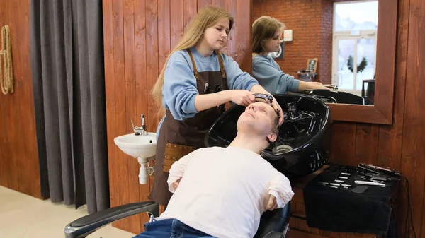 A hairdresser girl washes the hair of a man with limited opportunities in a beauty salon.