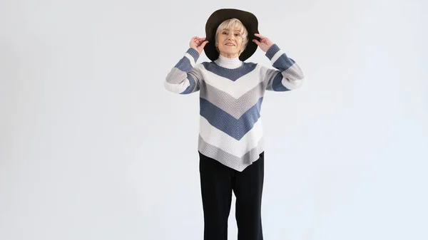 一位老妇人戴着一顶白色背景的帽子试穿 — 图库照片