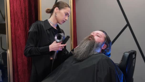 Ein Friseurmädchen Mit Einem Haartrockner Den Langen Bart Eines Mannes — Stockvideo