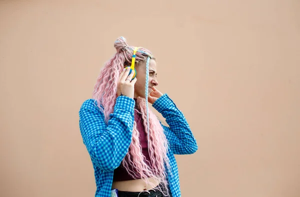 ピンクのロングヘアとブルーのシャツを着た幸せな若い女性 明るい背景のヘッドフォンを持つ女の子 広告テキストのための空スペース — ストック写真