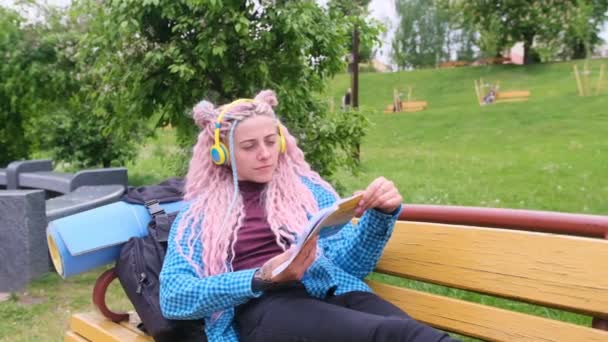 公園のベンチに横たわる本を読んでいるピンクの髪の女の子 — ストック動画