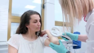 Klinikte tıbbi büyüteç kullanan bir kadın dermatolog hastanın derisini muayene ediyor..